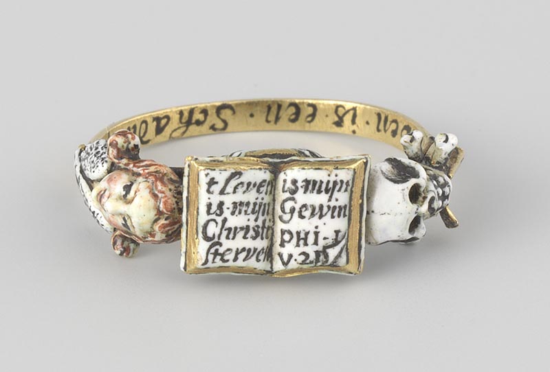 An inscribed ring decorated with an open book, an angel head, and a skull.