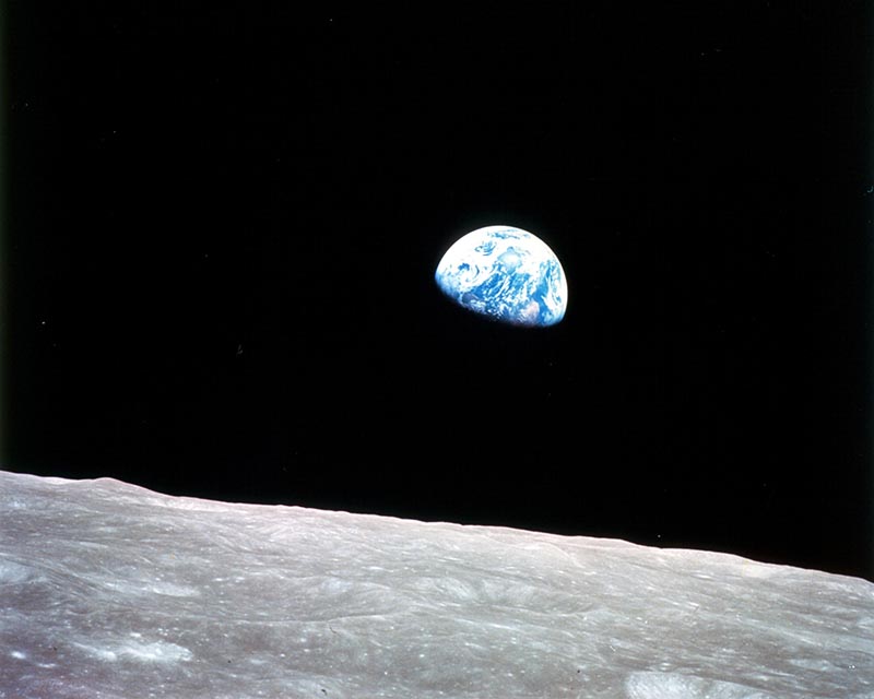 In the foreground, the surface of the moon, and in the background, Earth, partly shadowed on its southern hemisphere.