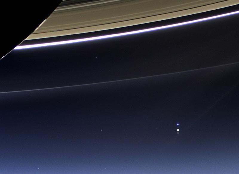 Part of the planet Saturn, with a pointer identifying a small white spot in the distance.